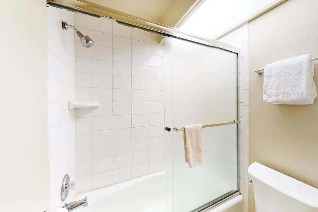 Un baño alicatado con ducha, mampara de vidrio y toallas.