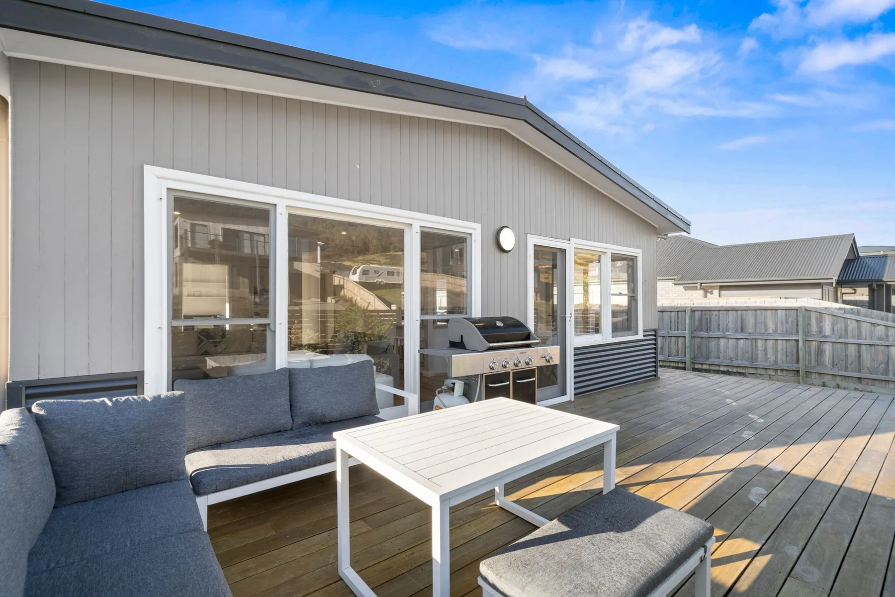 An outdoor deck with seating, a low table, and a grill beside the house.
