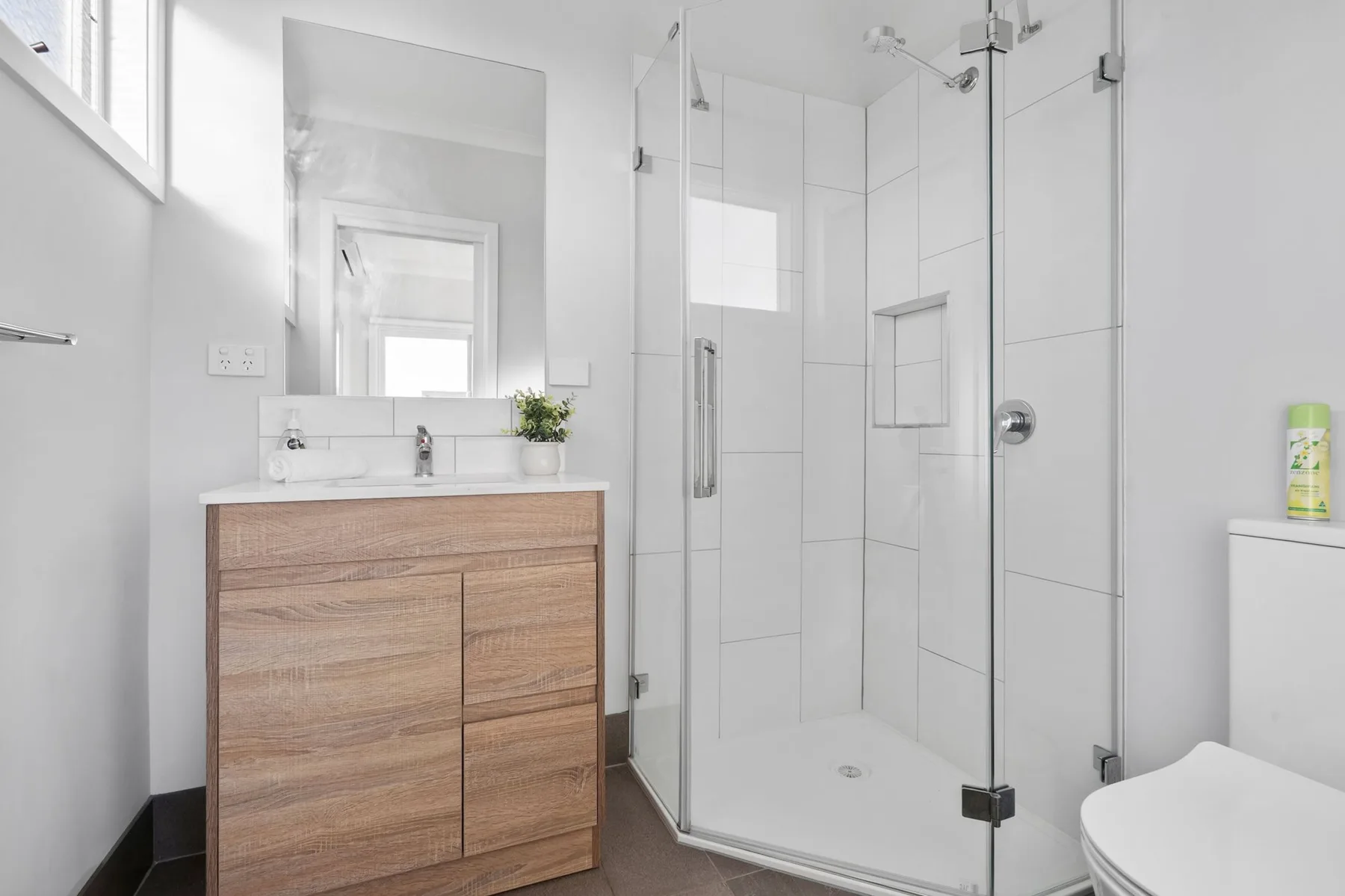 A bright bathroom with a wood vanity and glass shower.