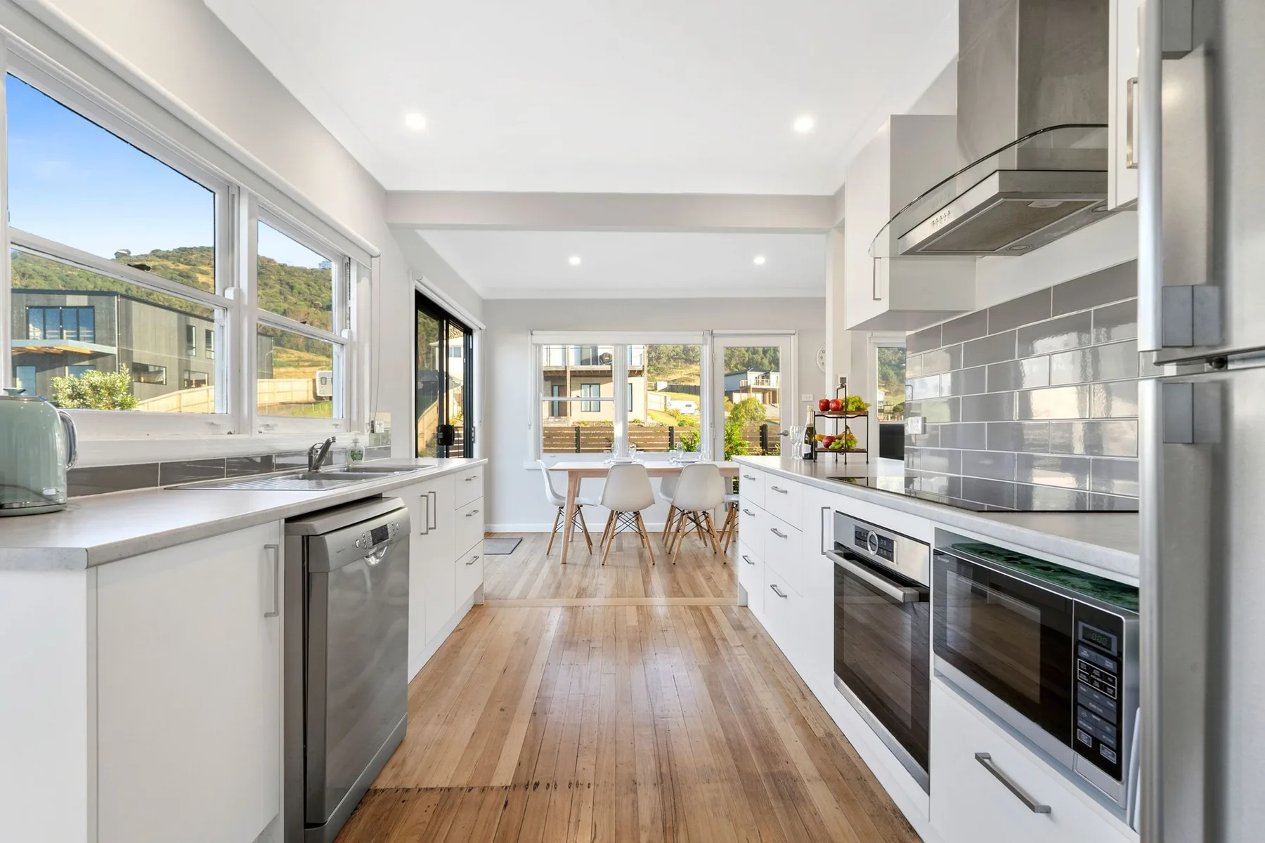 A bright kitchen with white cabinets and a long wooden floor.