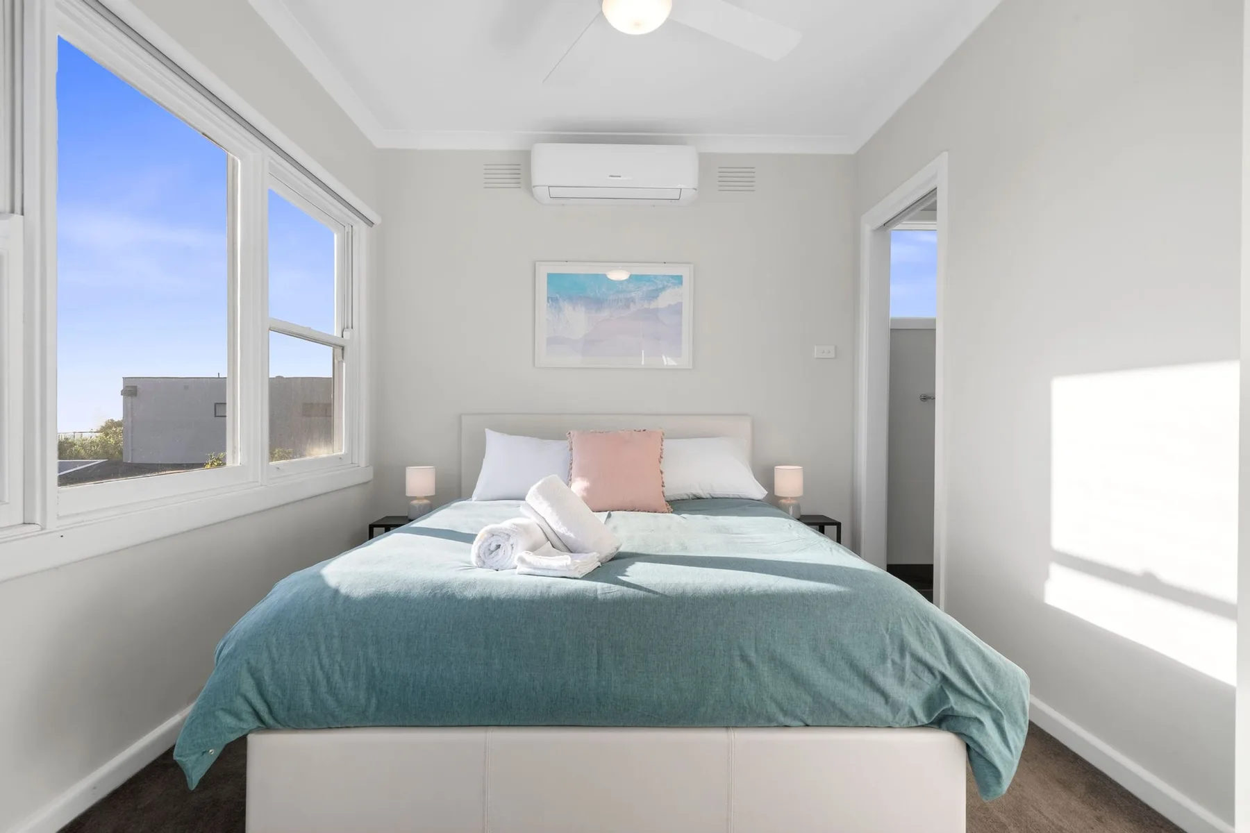 A bright bedroom with a bed beneath a framed picture.