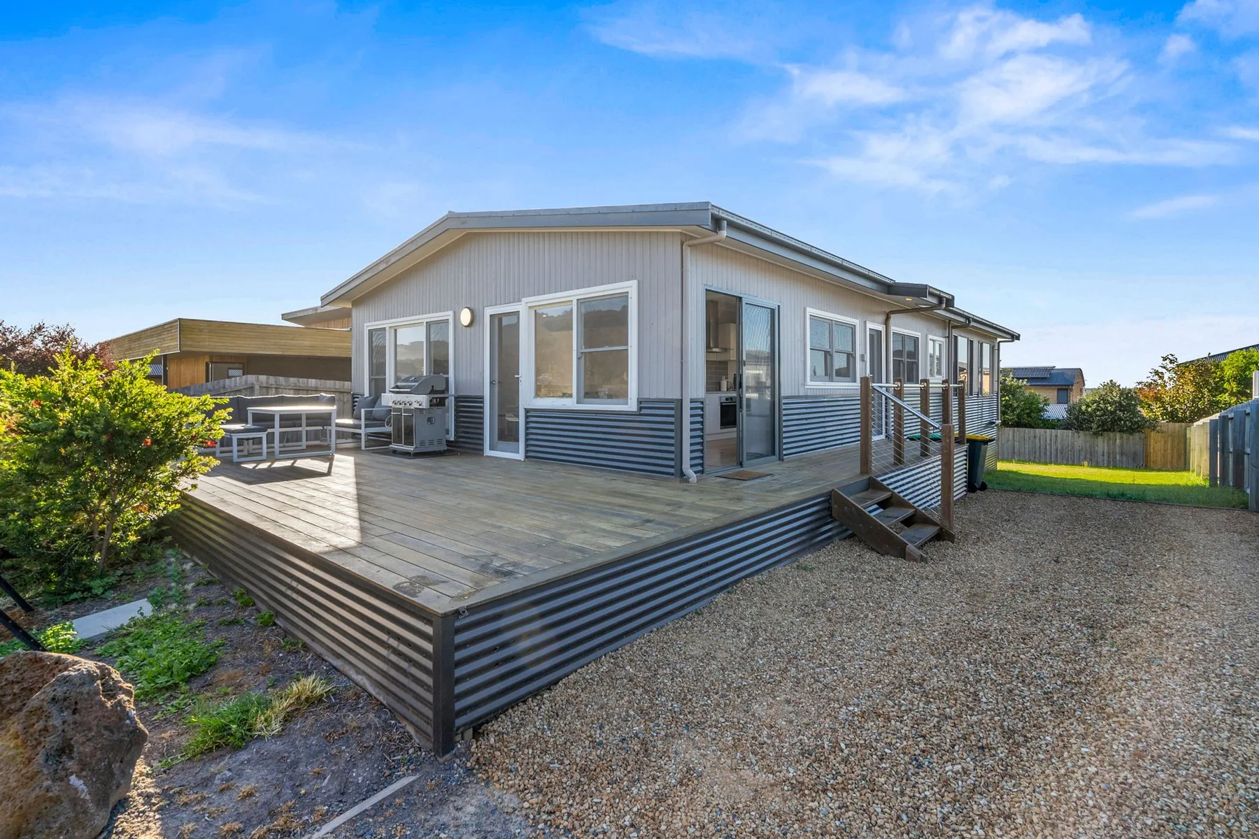 A coastal house with a raised wooden deck and gravel yard.