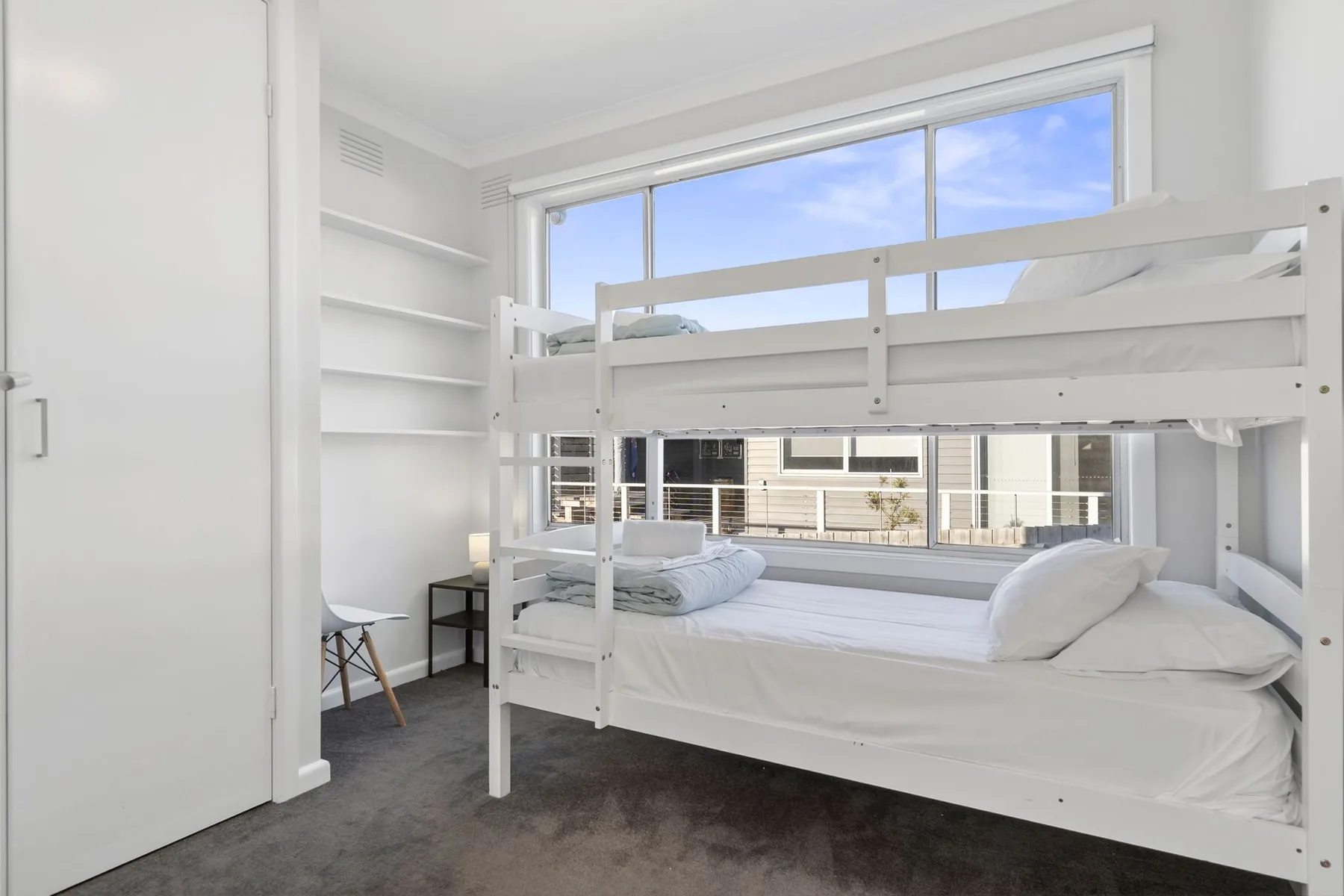 A bright bedroom with a white bunk bed beneath large windows.