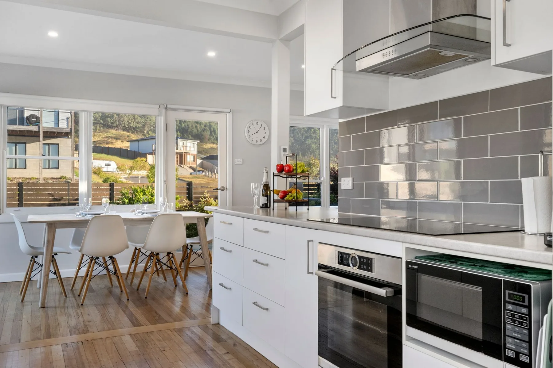 A bright kitchen and dining area with large windows and white cabinetry.