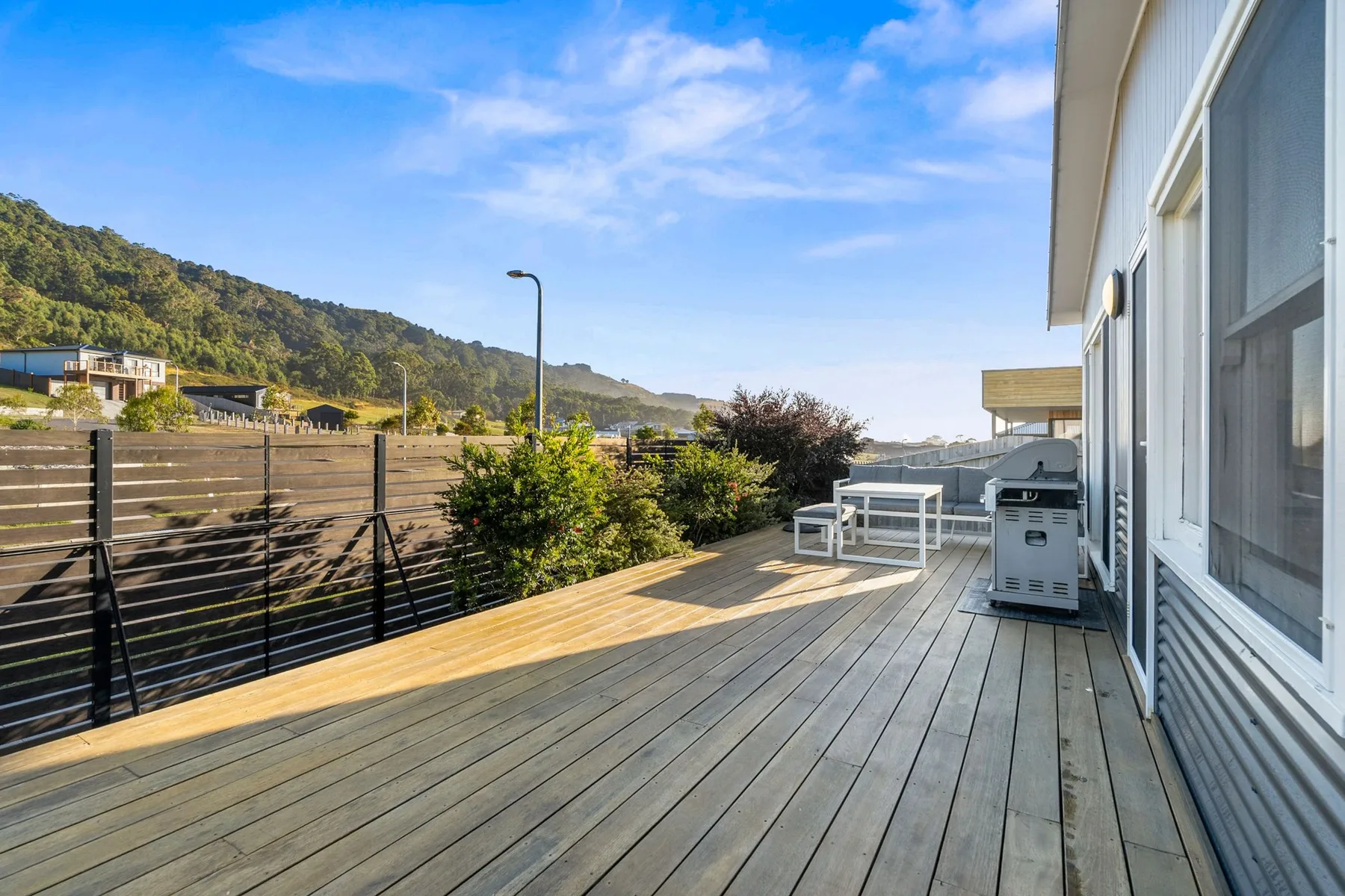 A wooden deck runs alongside the house, with outdoor seating and a grill.
