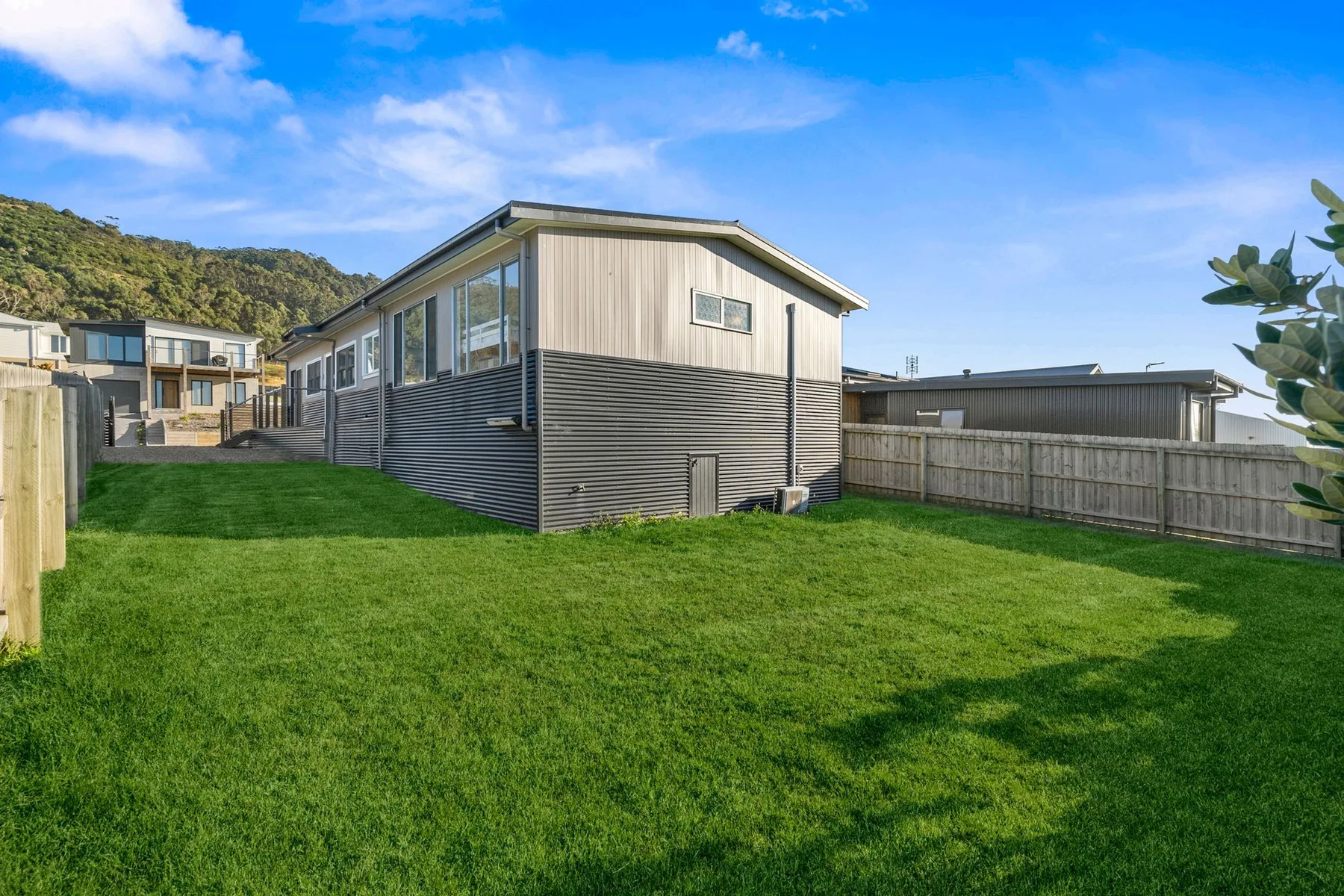 A modern building stands beside a broad green lawn under a blue sky.