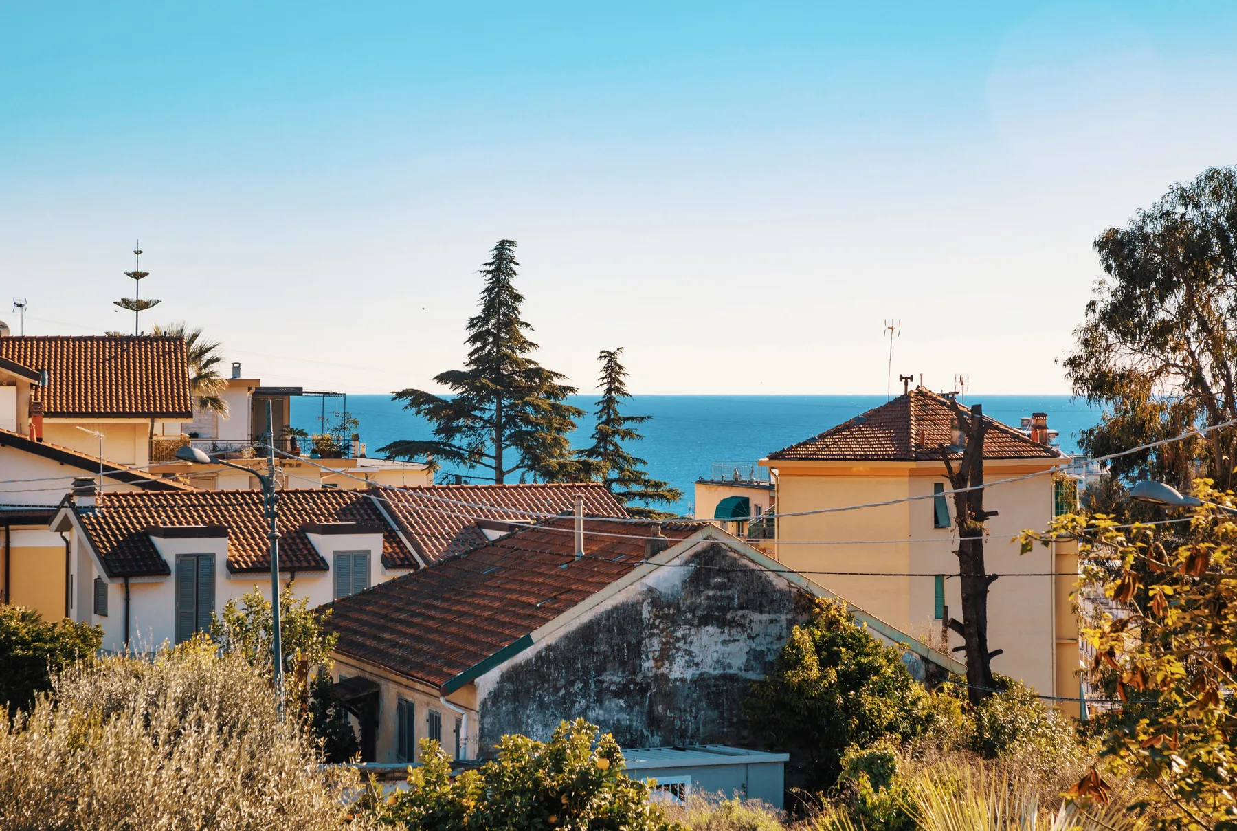 A coastal neighborhood of tiled-roof buildings overlooks the blue sea.
