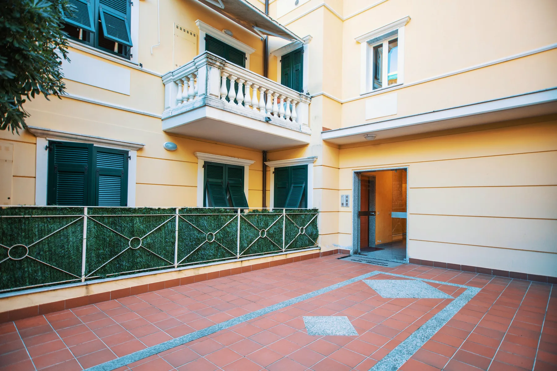 A paved courtyard beside a pale building, with windows and a balcony.