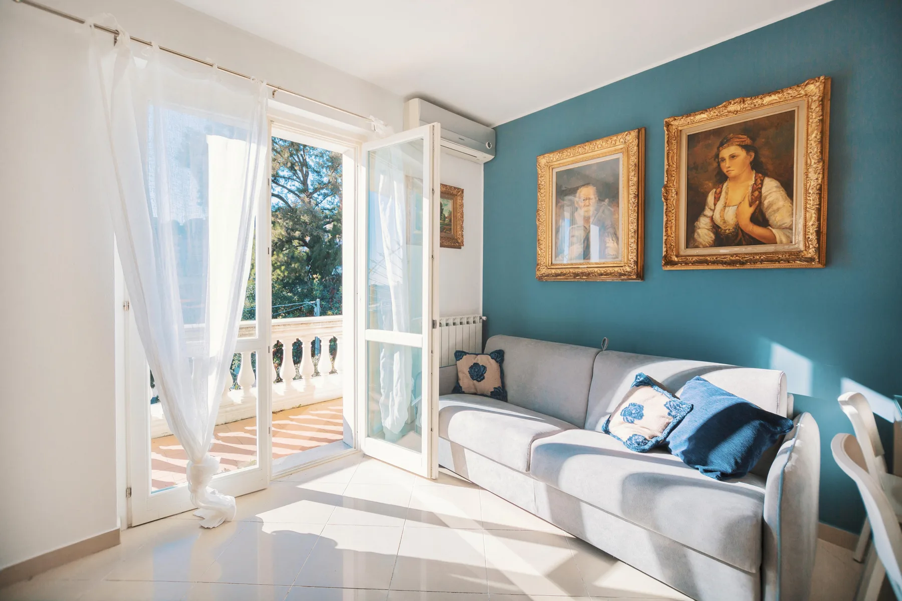 A bright living room with a gray sofa beside open balcony doors.