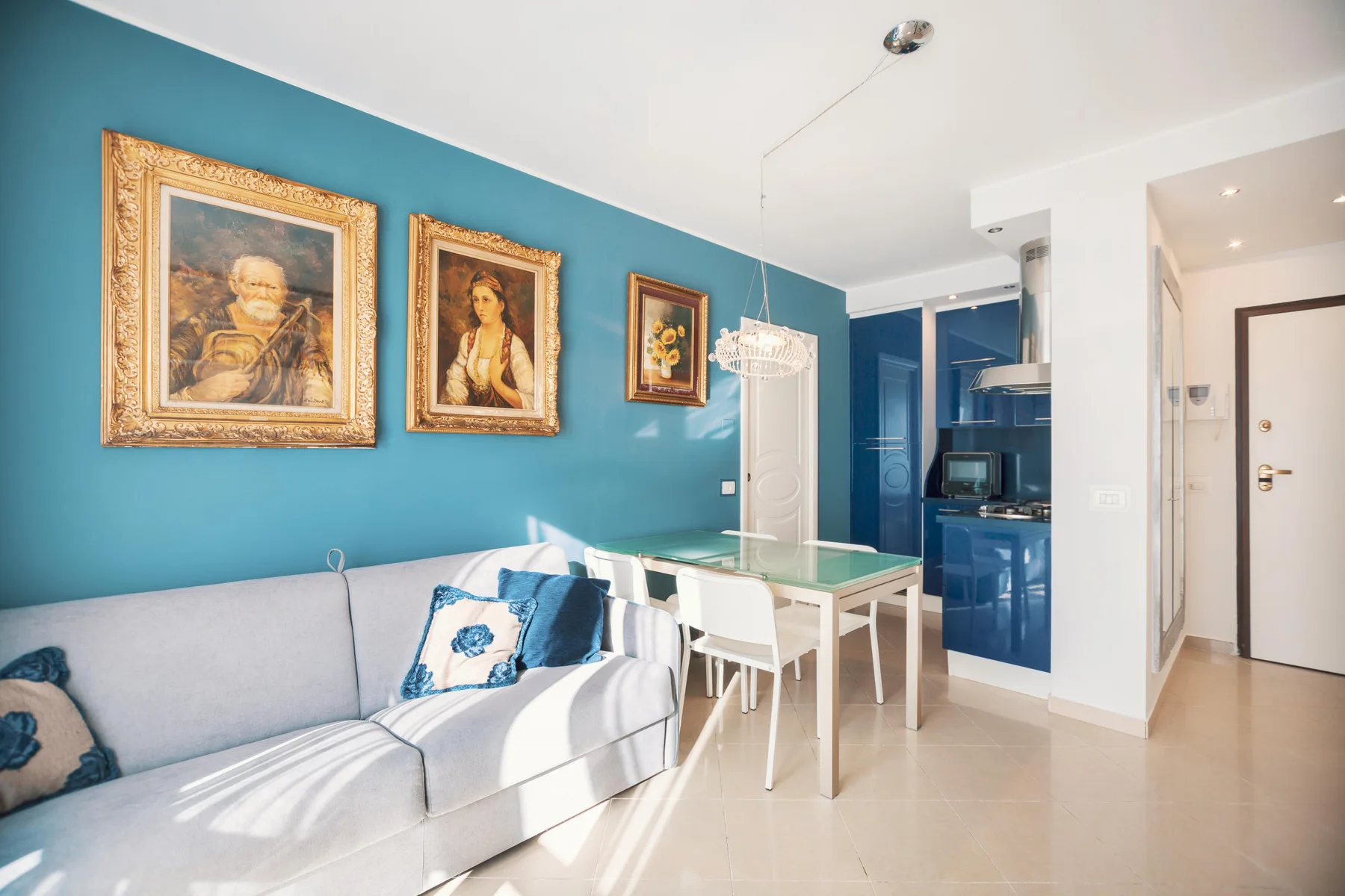 A bright living and dining area with a sofa, table, and blue kitchen cabinets.