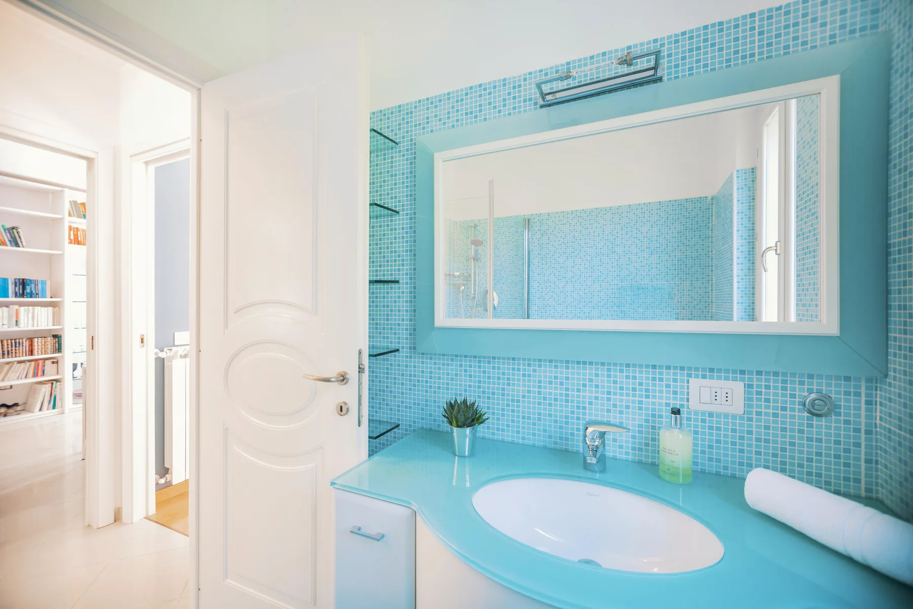 A bright bathroom with a turquoise tiled vanity and a large mirror.