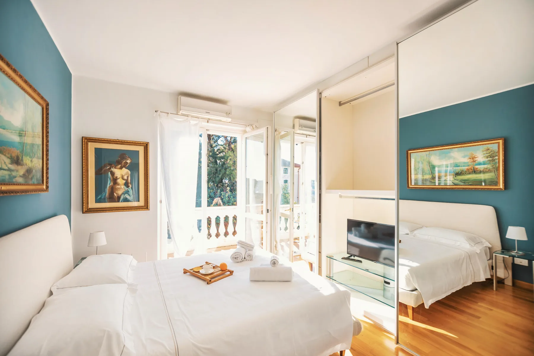 A bright bedroom with a bed beside tall windows and mirrored closet doors.