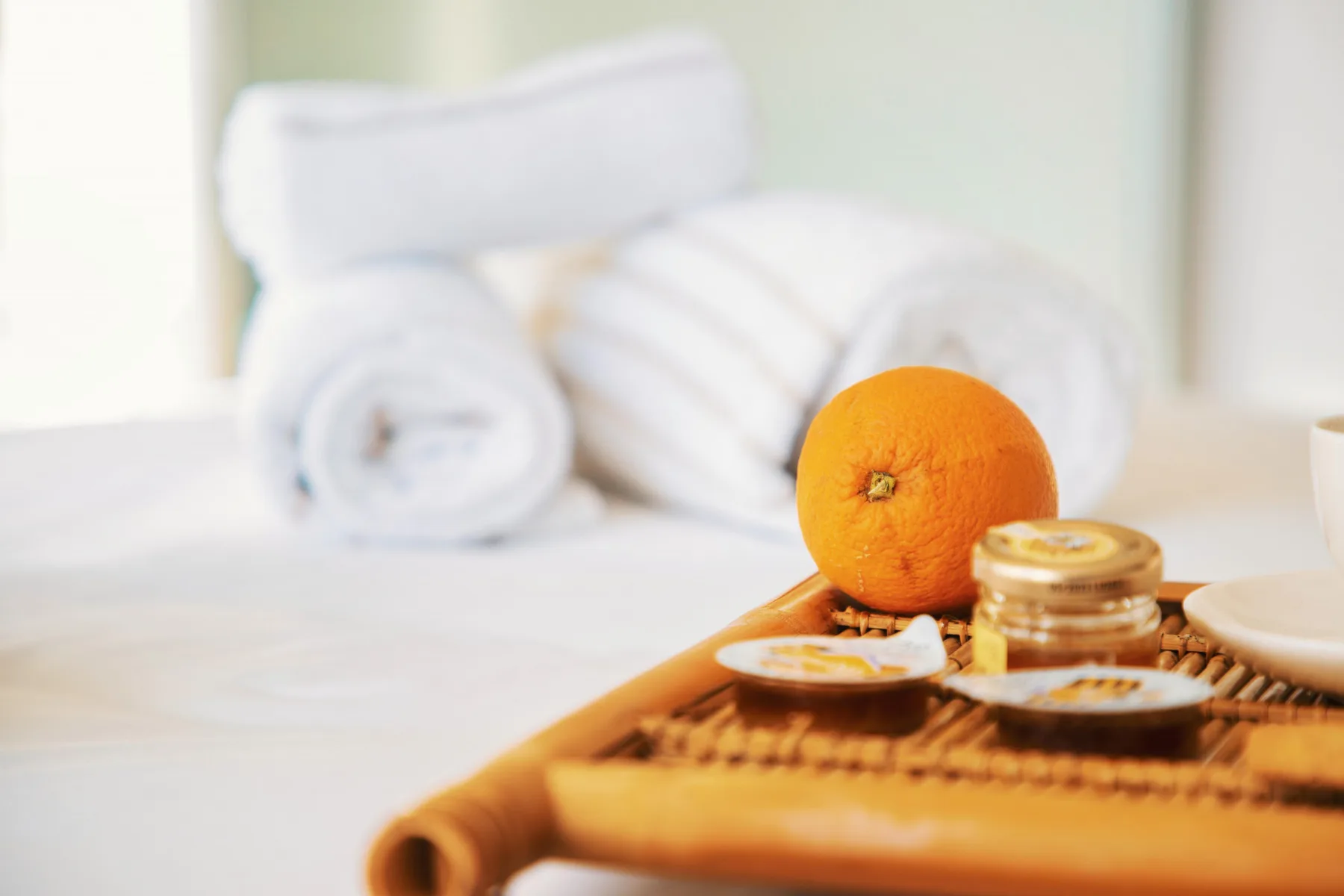 A bed with neatly arranged white towels and an orange on a tray.