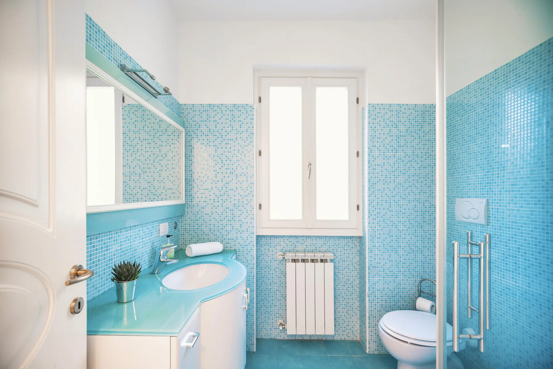 A bright bathroom with blue mosaic tile, a sink, and a shower.