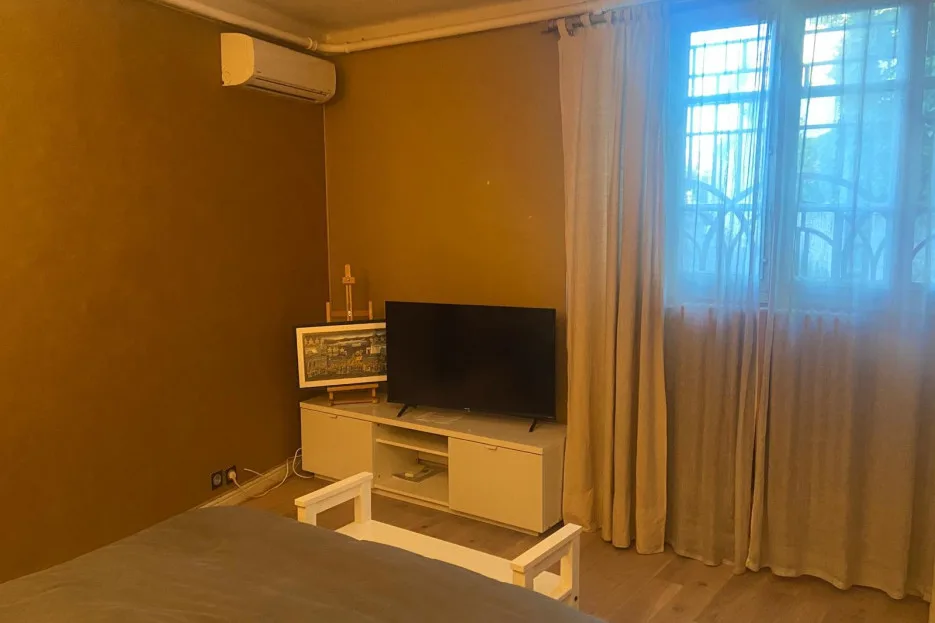 A bedroom with a television on a low stand beside a curtained window.