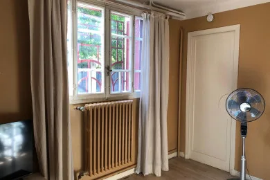 A room with a window, radiator, white door, and standing fan.