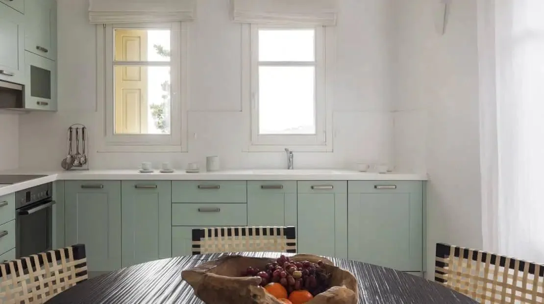 Una cocina luminosa con armarios verde claro y una mesa de comedor de madera.