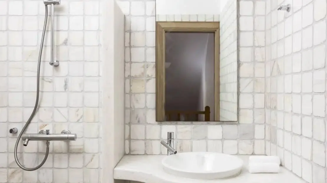 Un tocador de baño con azulejos, lavabo, espejo y ducha de pared.