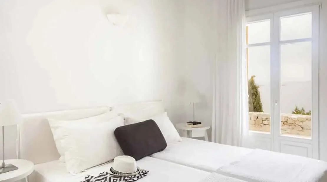 Un dormitorio luminoso con ropa de cama blanca y puertas altas de vidrio.