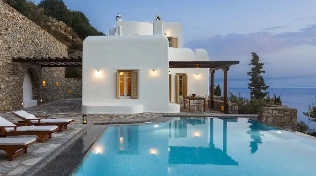 A poolside scene with lounge seating and a white building beside the sea.