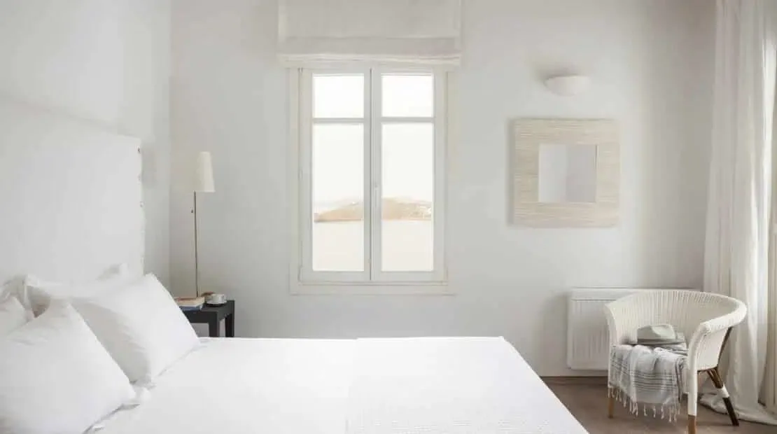 Un dormitorio luminoso con una cama blanca junto a una ventana alta.