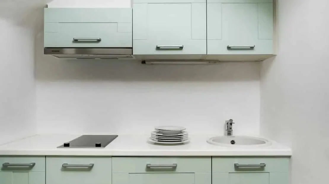 Una cocina compacta con gabinetes claros, una placa de cocina y un fregadero.
