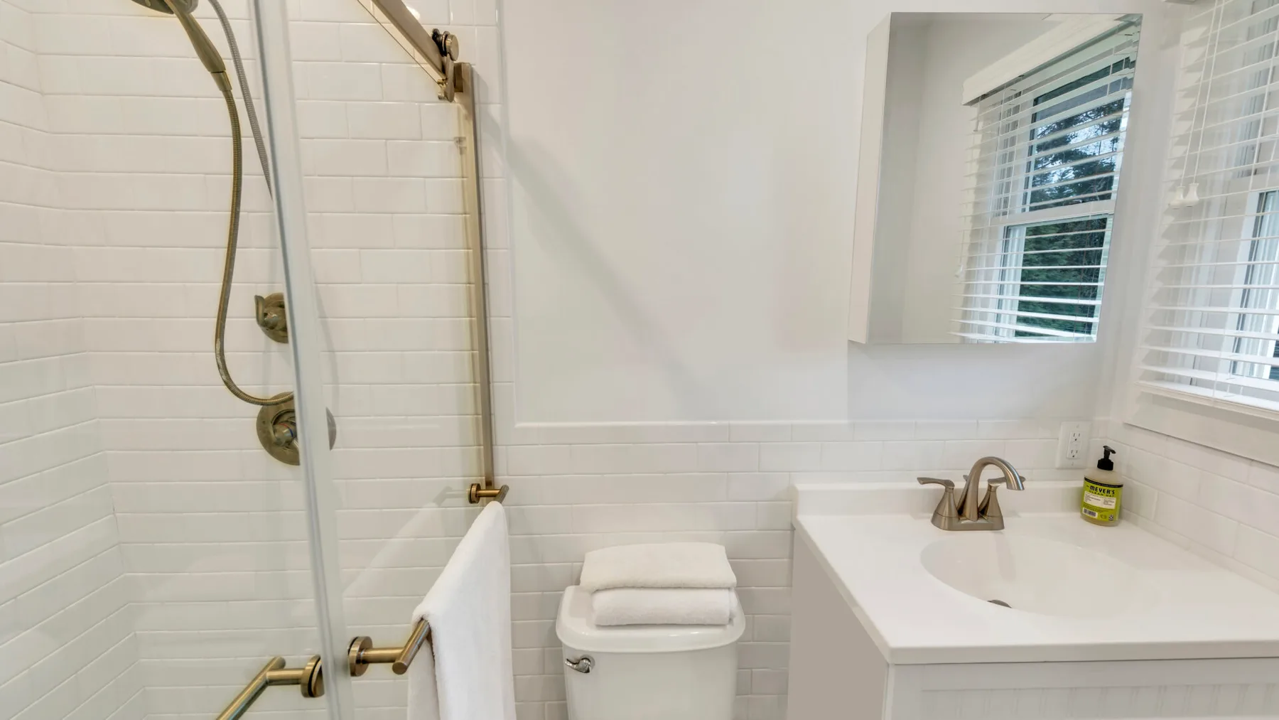 Un baño luminoso tiene una ducha con azulejos junto a un lavabo y una ventana.