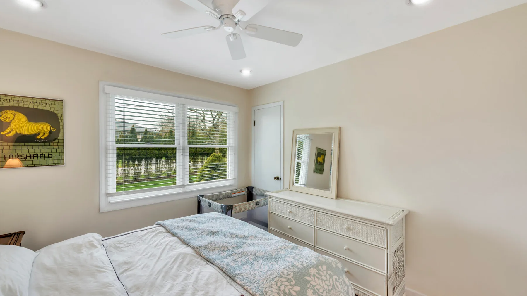 Un dormitorio luminoso con cama, cómoda y ventanas con vistas a la vegetación.