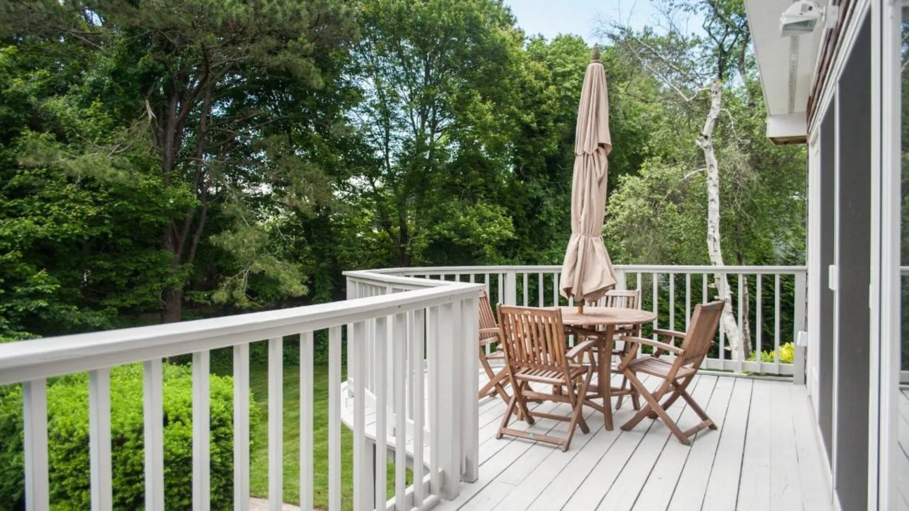 A wooden deck with outdoor seating and an umbrella overlooks a green yard.