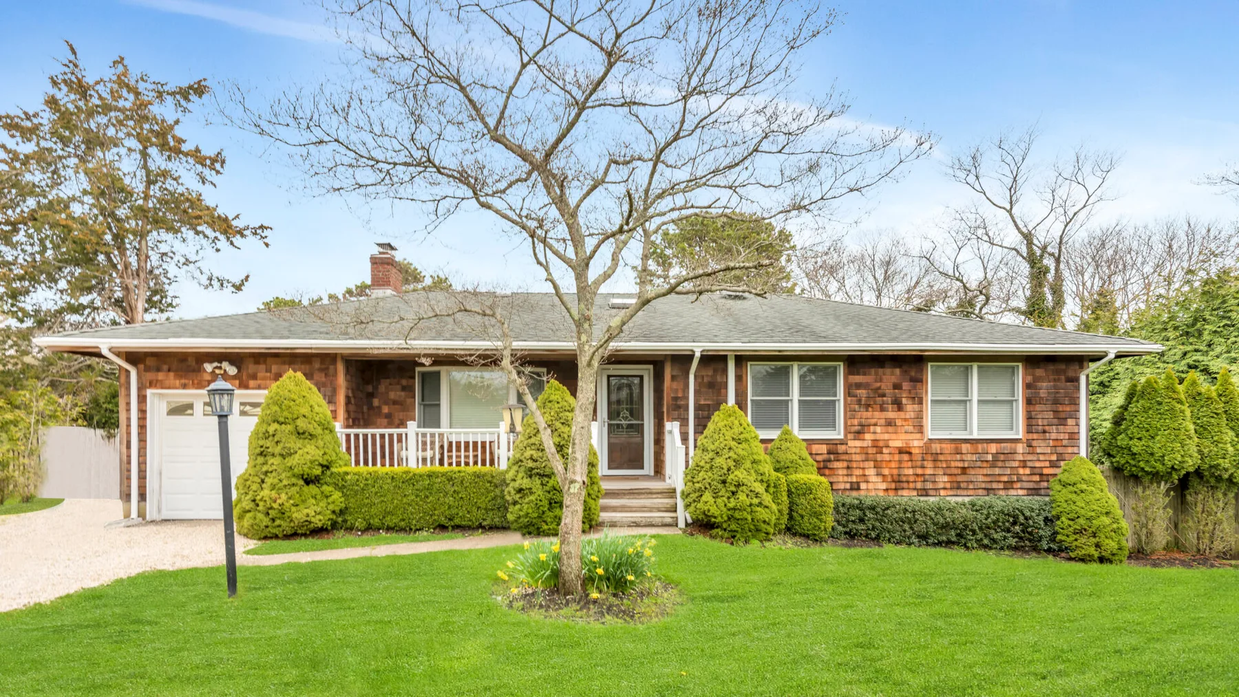 A single-story brick house with a front lawn and several shrubs.