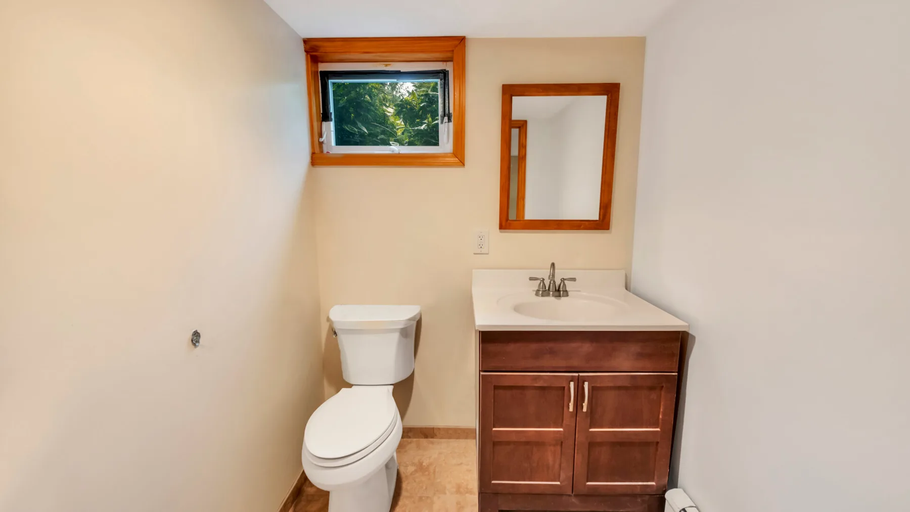 Un baño pequeño con un mueble de madera y una ventana sobre el inodoro.