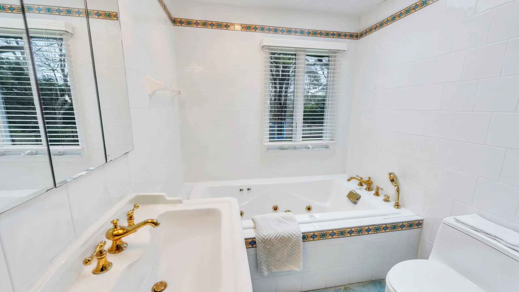 Un baño de azulejos blancos con bañera, lavabo y ventana.