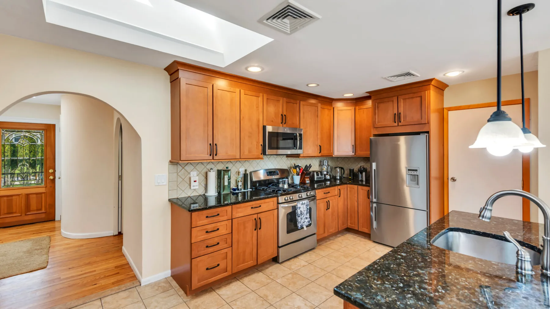 Una cocina con gabinetes de madera, electrodomésticos de acero inoxidable y una encimera oscura.