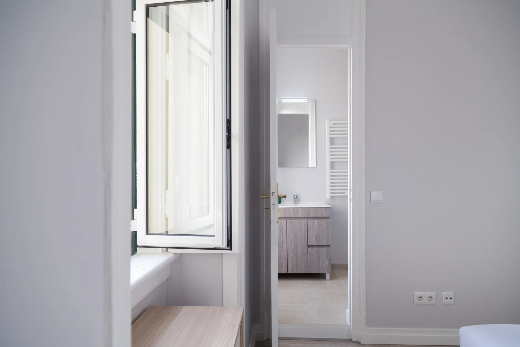 Una habitación luminosa con una ventana abierta y un baño visible a través de la puerta.