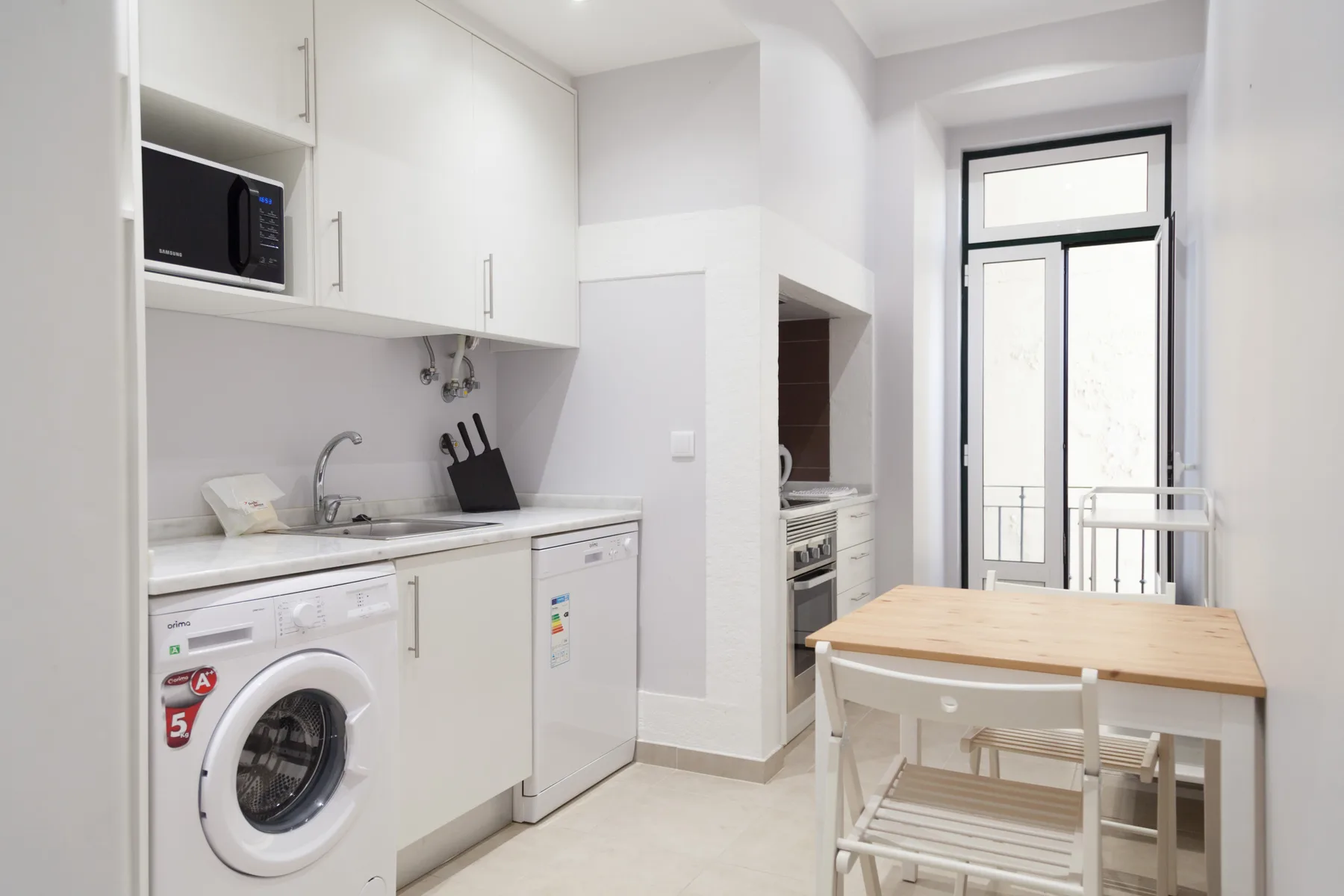 Una cocina luminosa con armarios blancos, una lavadora y una mesa de comedor de madera.