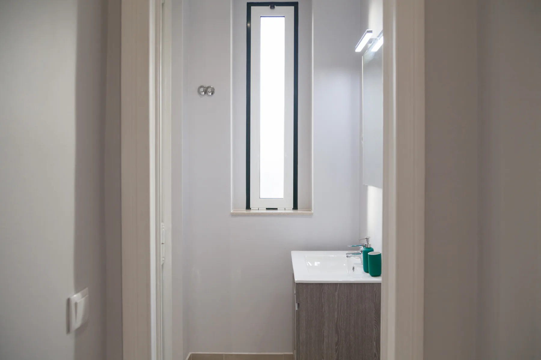 Un baño con un lavabo bajo una ventana estrecha.