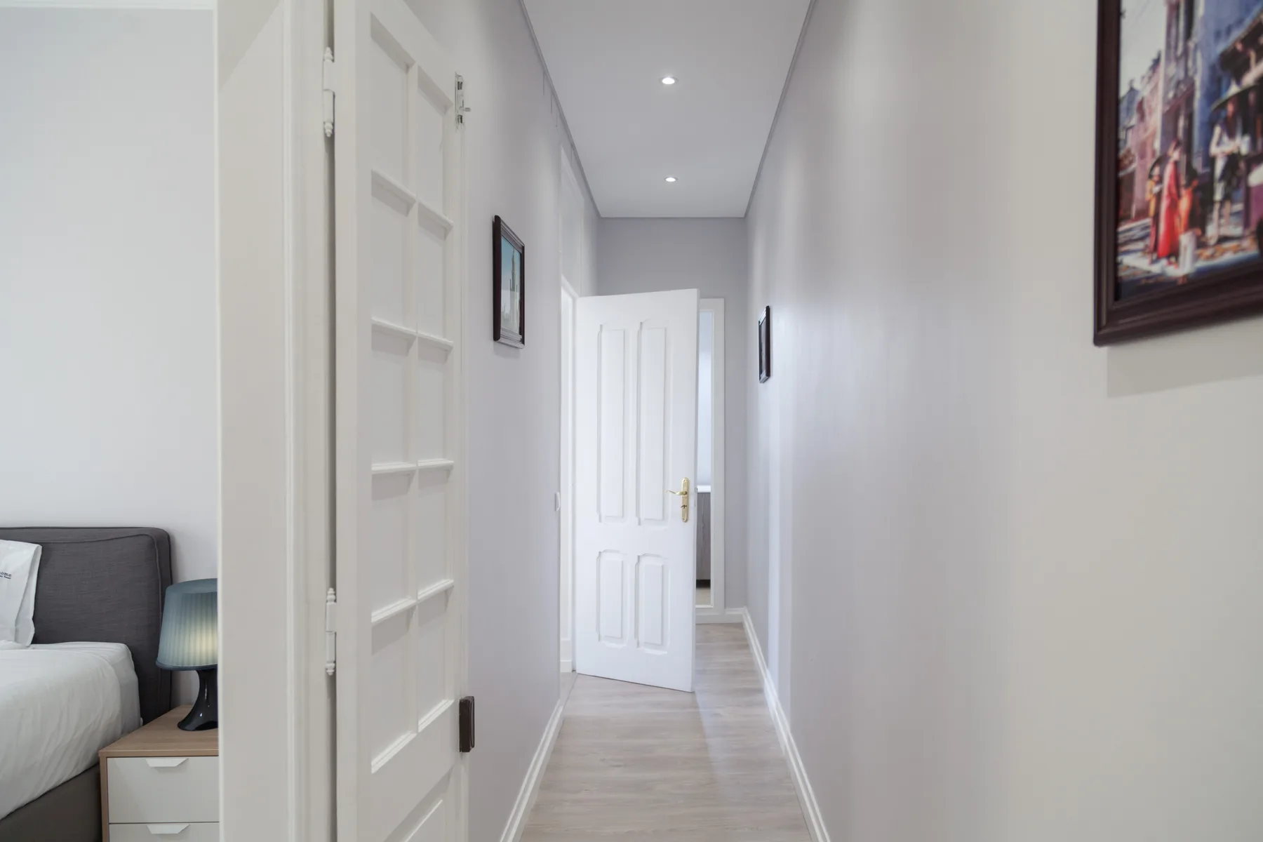 Un pasillo luminoso de apartamento con puertas blancas y cuadros enmarcados.