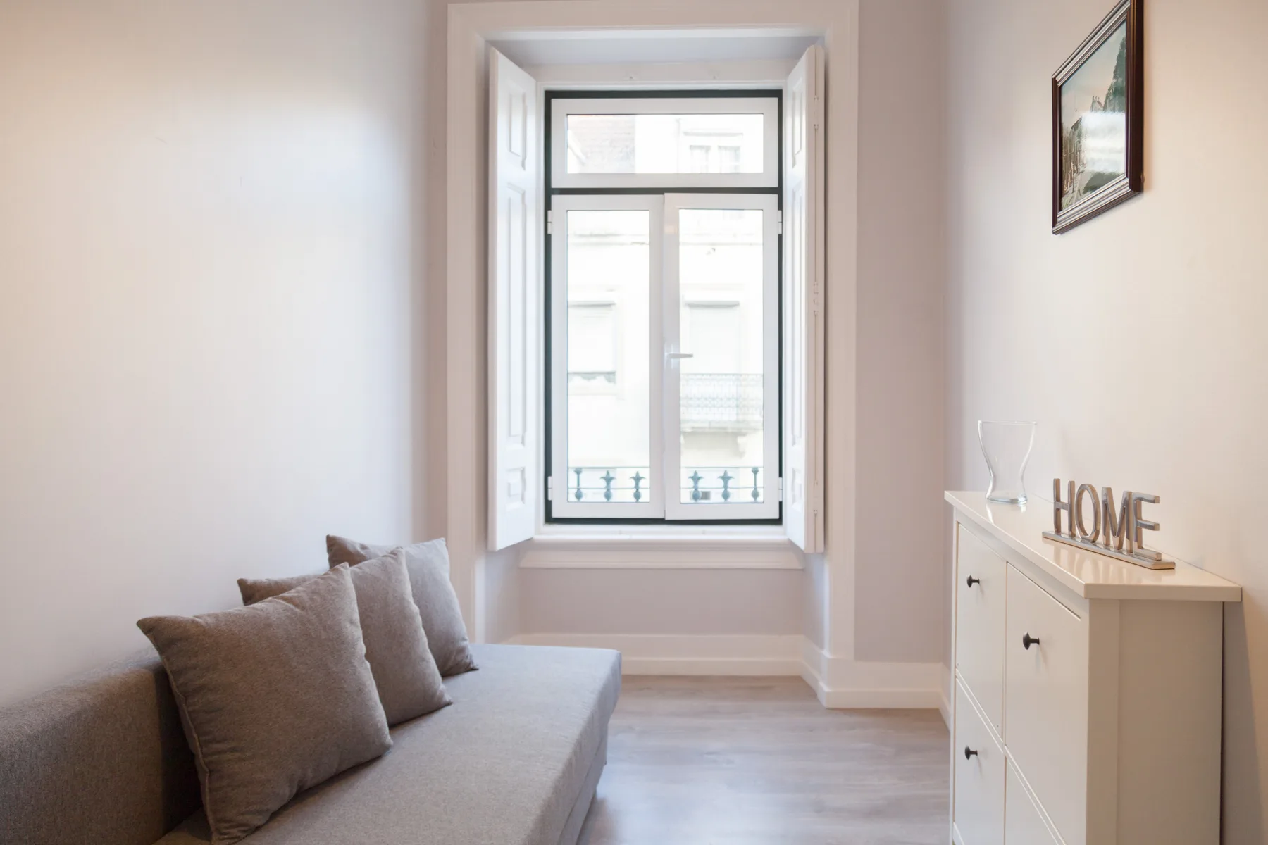 Una sala luminosa con un sofá gris junto a una ventana.