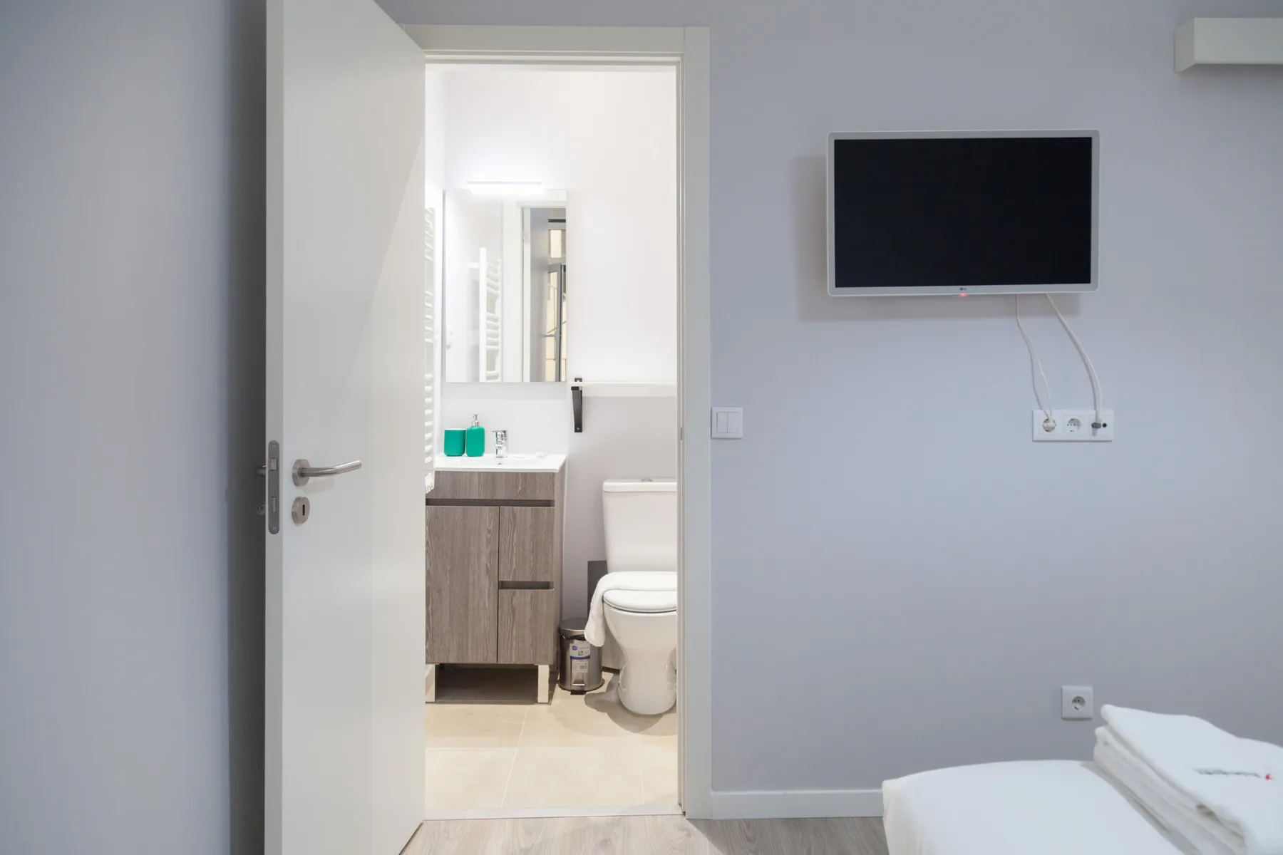 Un dormitorio con un televisor en la pared y una puerta abierta al baño.
