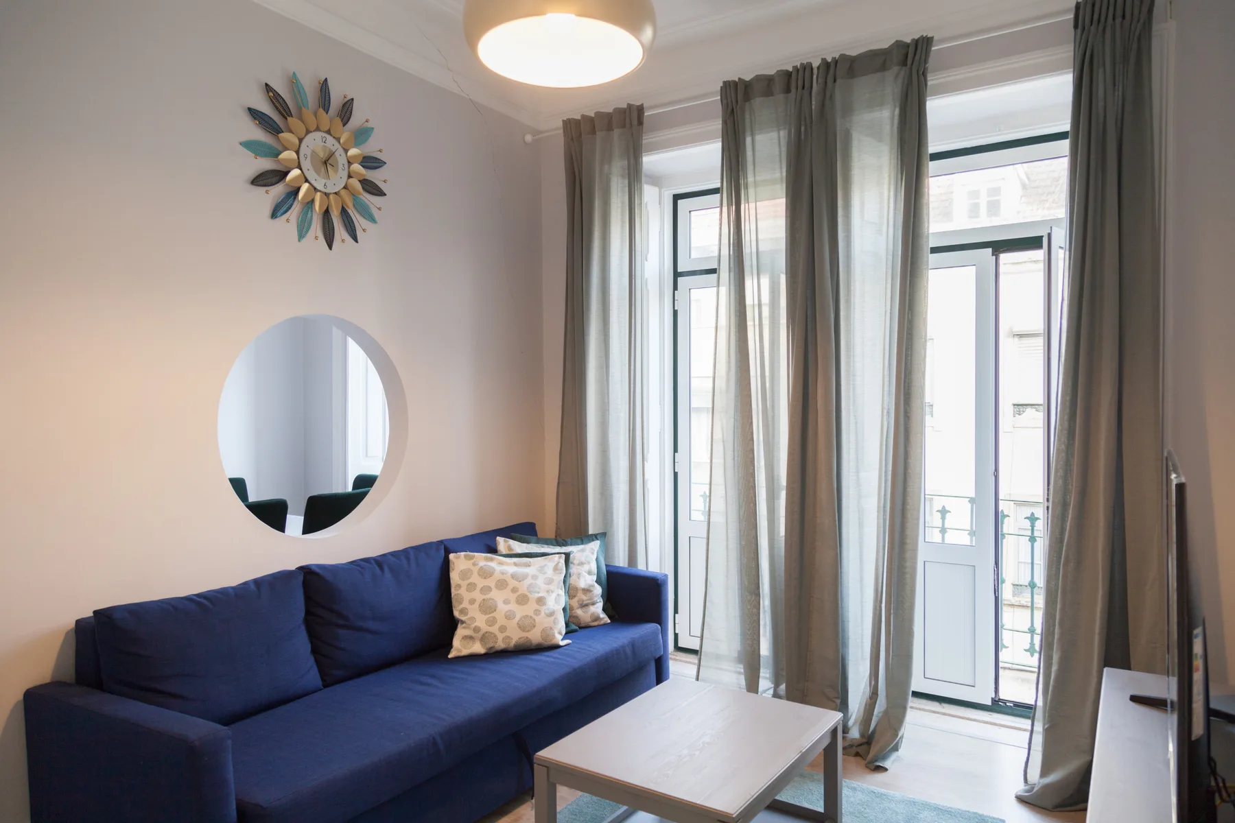 Sala de estar con asientos azules y ventanas altas cubiertas por cortinas translúcidas.