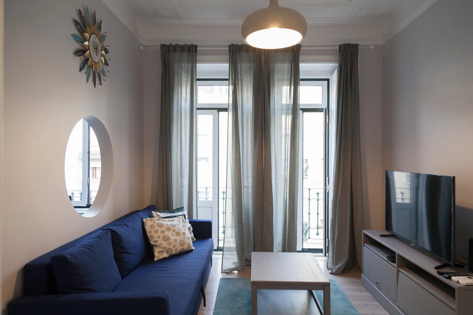 Sala de estar con asientos azules, una mesa de centro y ventanas altas.