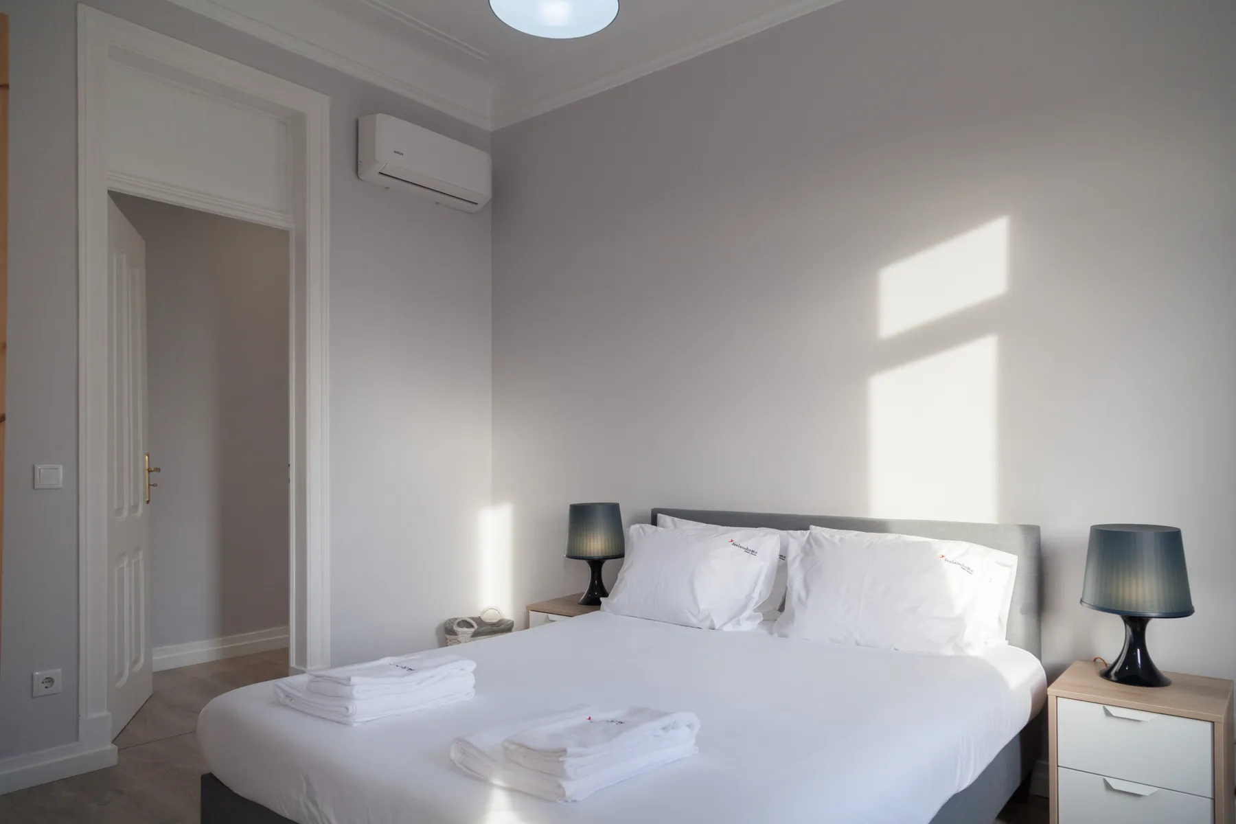 Un dormitorio luminoso con una cama blanca y mesitas de noche.