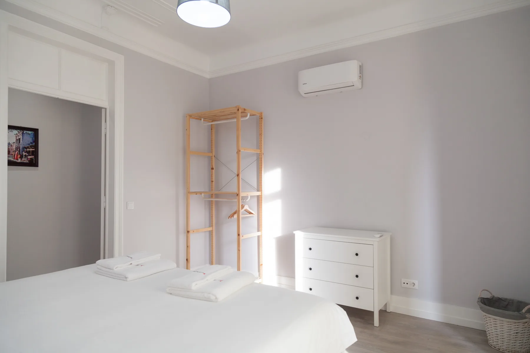 Un dormitorio luminoso con una cama y un perchero abierto de madera.