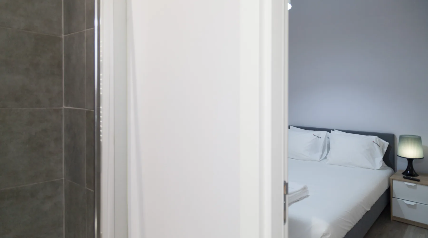 Un dormitorio con ropa de cama blanca y una mesita se ve a través de una puerta abierta.