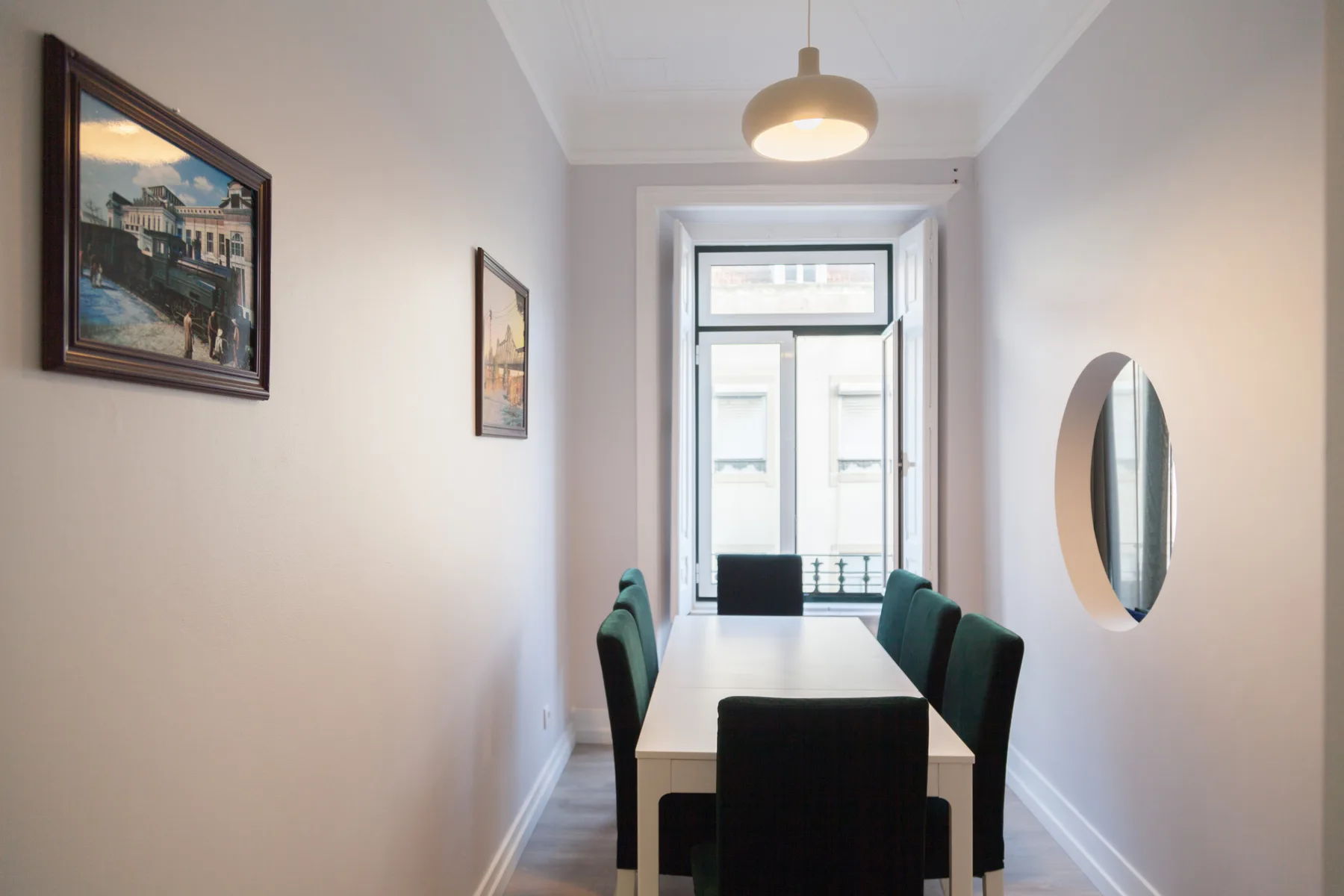 Un comedor estrecho con una mesa, asientos y cuadros en la pared.