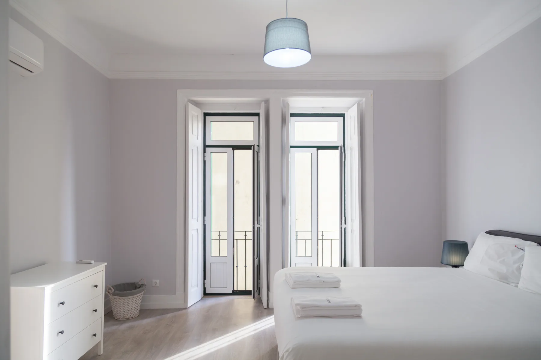 Un dormitorio luminoso con una cama junto a ventanas altas.