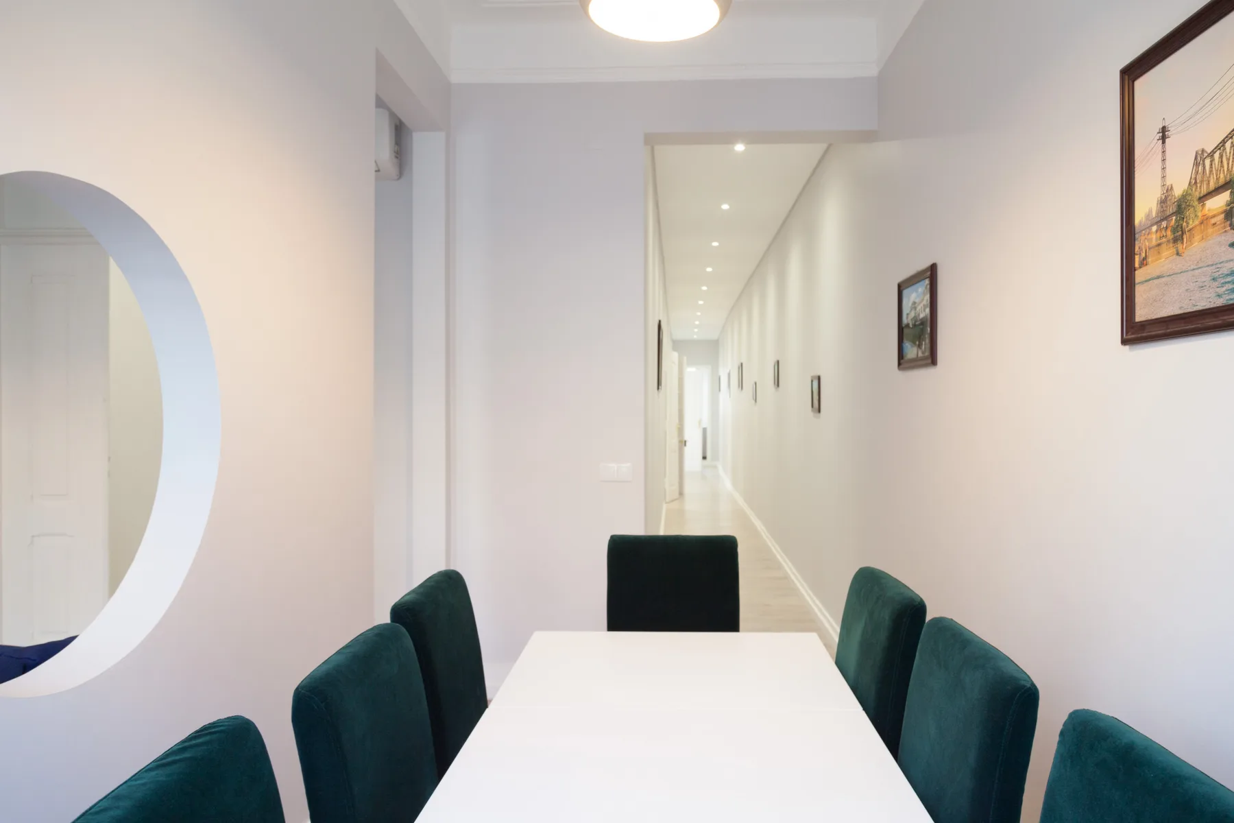 Comedor con una mesa larga y asientos tapizados junto a un pasillo.
