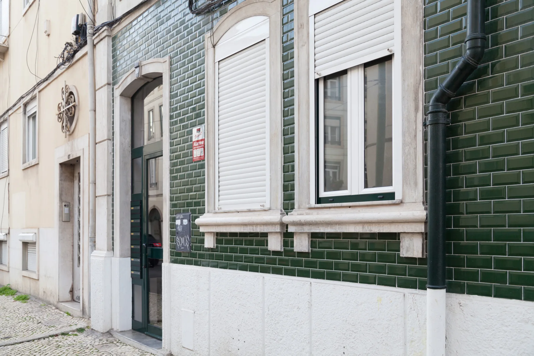 Fachada de un edificio a la calle, con azulejos verdes, ventanas y una entrada.