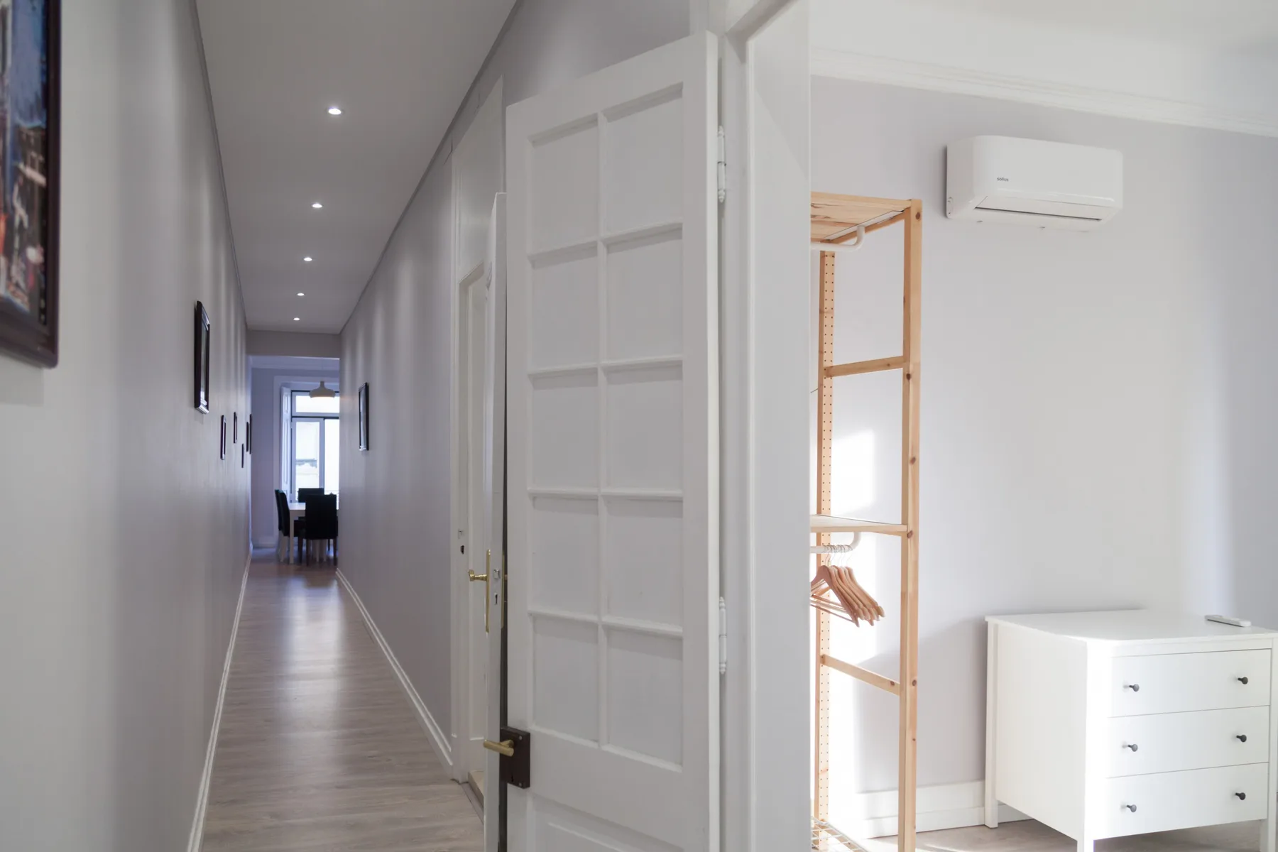 Un pasillo luminoso da a una habitación con una cómoda y un perchero.