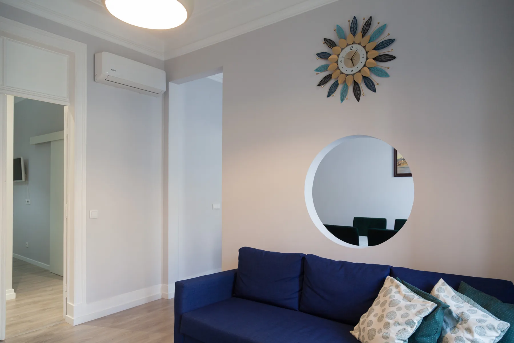 Una sala de estar con un sofá azul, cojines estampados y un espejo redondo.